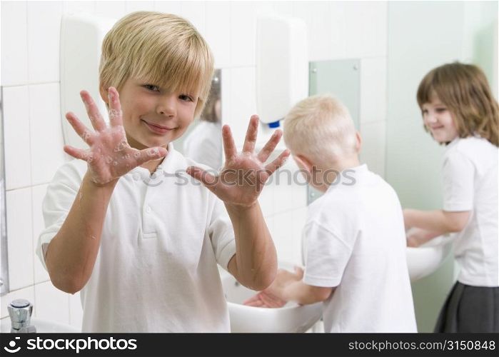 Students in bathroom at sinks washing hands with one holding up soapy hands (selective focus)