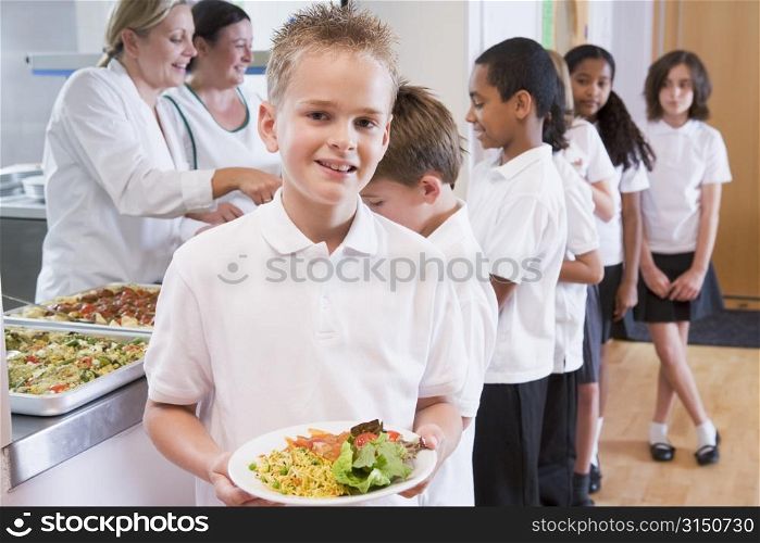 Students in cafeteria line with one holding his healthy meal and looking at camera (depth of field)