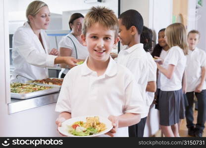 Students in cafeteria line with one holding his healthy meal and looking at camera (depth of field)