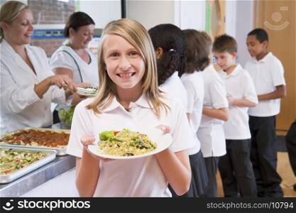 Students in cafeteria line with one holding up her healthy meal and looking at camera (depth of field)