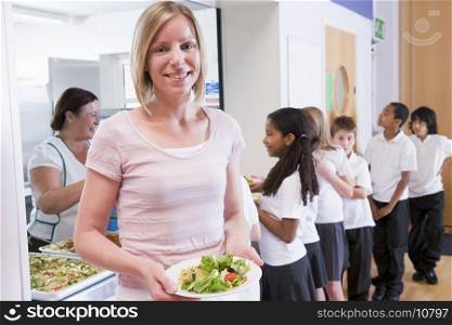 Students in cafeteria line with teacher holding her healthy meal and looking at camera (depth of field)