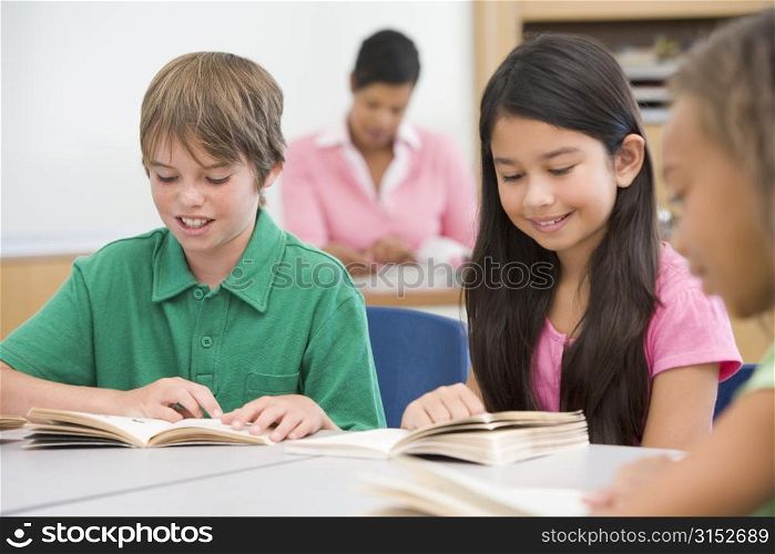 Students in class reading with teacher in background (selective focus)