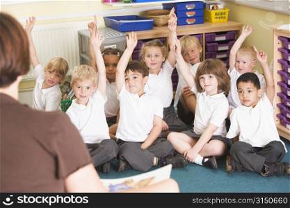 Students in class sitting on floor volunteering for teacher (selective focus)