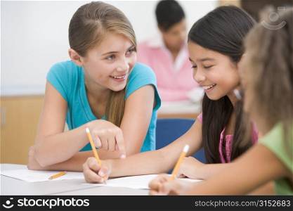 Students in class writing and talking with teacher in background (selective focus)