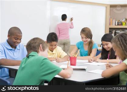 Students in class writing with teacher at front board