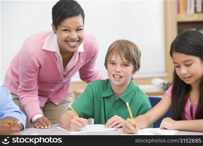 Students in class writing with teacher helping