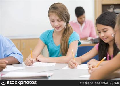 Students in class writing with teacher in background (selective focus)