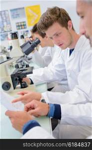 Students in lab using microscopes, reading paperwork