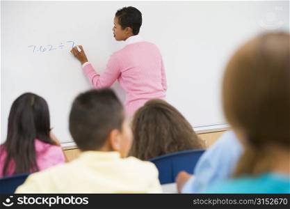 Students in math class with teacher writing on front board (selective focus)