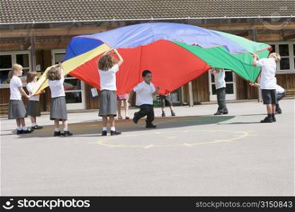 Students outdoors during recess playing with a parachute