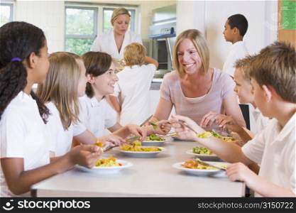 Students sitting at cafeteria table eating lunch with teacher