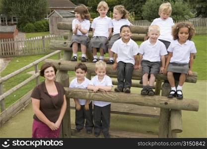 Students sitting outdoors on wooden structure with teacher standing beside them