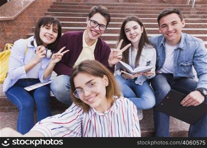 students sitting stairs gesturing two fingers looking camera