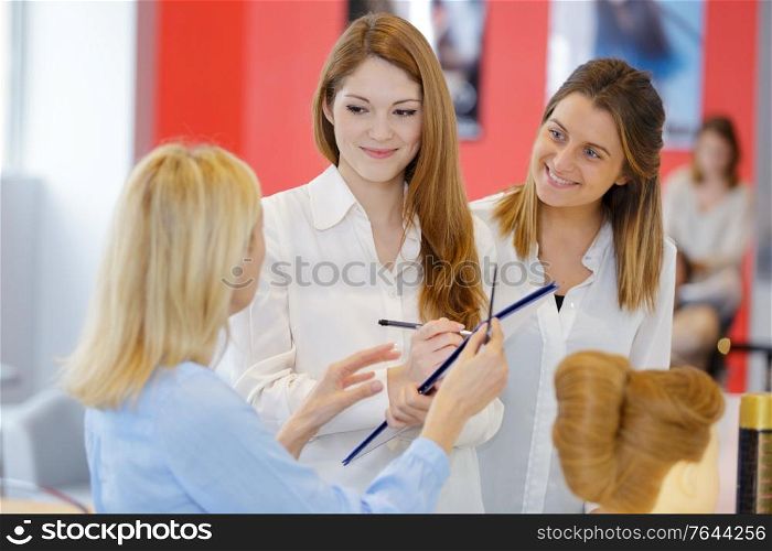 students taking notes as hairdresser demonstrates style on mannequin