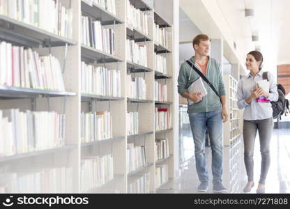 Students talking while walking by bookshelf at university library