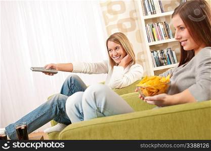 Students - Two female teenager watching television and eating crisps in modern lounge