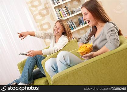 Students - Two female teenager watching television and eating crisps in modern lounge
