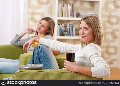 Students - Two smiling female teenager watching television together, eating crisps