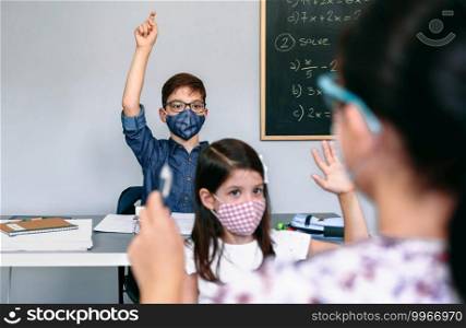 Students with face masks raising their hands at school with their female teacher