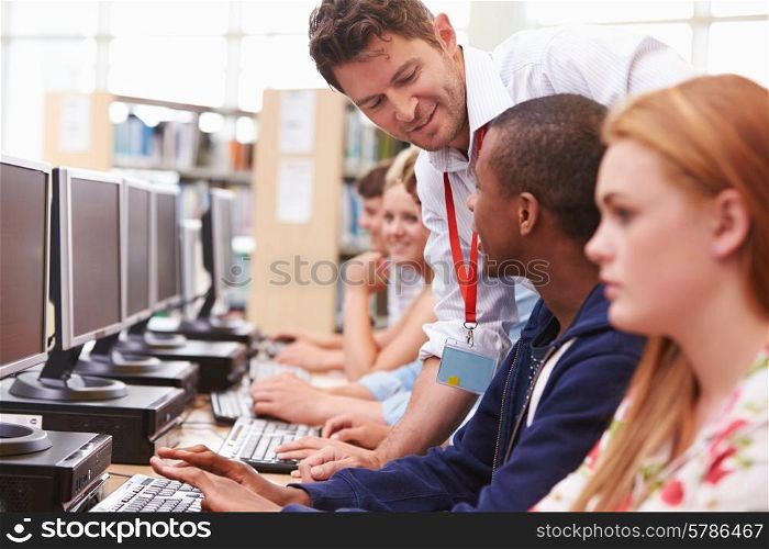 Students Working At Computers In Library With Teacher