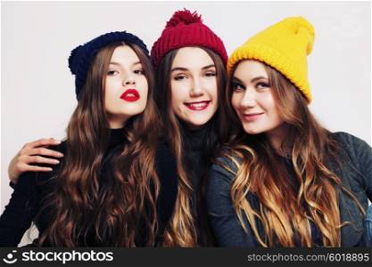 Studio fashion portrait of a group of three young beautiful model posing in winter leather shoes, warm clothes and colorful knitted caps. Friends having fun. Consumer concept, winter fashion