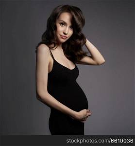 Studio fashion portrait of beautiful pregnant woman in black dress. Happy pregnancy. Beauty and health