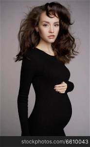 Studio fashion portrait of beautiful pregnant woman in black dress. Happy pregnancy. Beauty and health