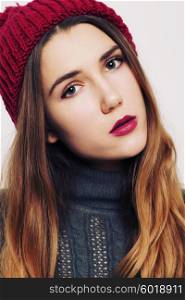 Studio fashion portrait of beautiful young woman wearing grey sweater and marsala color hat against white wall background. Consumer concept, winter fashion