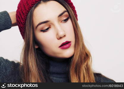 Studio fashion portrait of beautiful young woman wearing grey sweater and marsala color hat against white wall background. Consumer concept, winter fashion