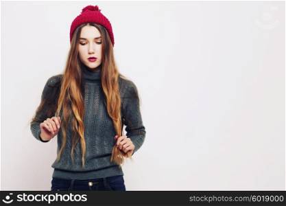 Studio fashion portrait of beautiful young woman wearing grey sweater and marsala color hat against white wall background. Consumer concept, winter fashion