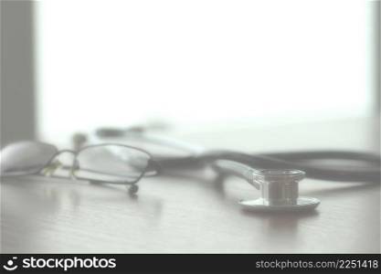 Studio macro of a stethoscope and glasses with shallow DOF evenly matched abstract on wood table background copy space