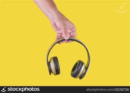 Studio photo with copy space with yellow background of a hand holding a brown wireless headphone. Hand of a person holding a brown wireless headphone in a yellow background