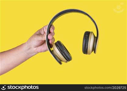 Studio photo with yellow background of a hand holding a brown wireless headphone. Person holding a brown wireless headphone in a yellow background