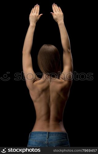 Studio photo, young, slim, athletic girl with a naked back in blue jeans held up his hands. Isolate on black.