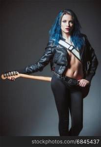 Studio portrait: a sexy rock girl with blue hair stands with electric guitar