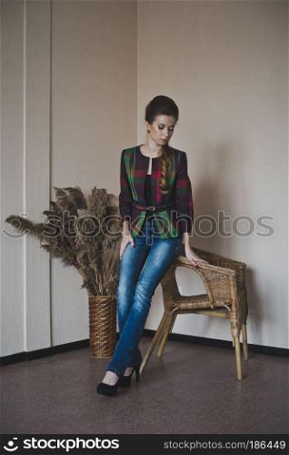 Studio portrait of a beautiful girl.. A beautiful girl stands near the chairs and the vase with reeds 4857.