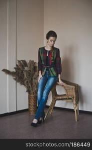 Studio portrait of a beautiful girl.. A beautiful girl stands near the chairs and the vase with reeds 4857.