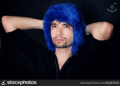 Studio portrait of a young Caucasian man in a blue winter hat on a black background