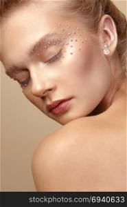 Studio Portrait of a young cute blonde model girl in art makeup with rhinestones. Portrait of cute blonde girl with art makeup