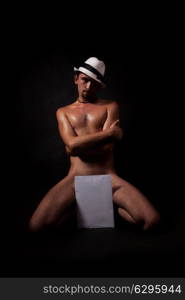 Studio portrait of a young naked man in a white hat on a black background