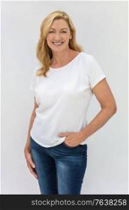 Studio portrait of an attractive middle aged blonde woman smiling on a white background wearing a white t-shirt and blue jeans