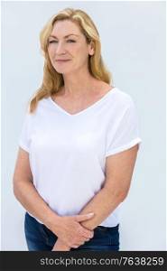 Studio portrait of an attractive middle aged blonde woman smiling on a white background wearing a white t-shirt and blue jeans