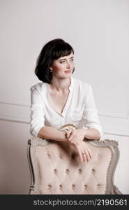 Studio portrait of attractive young woman with dark hair in white shirt and red pants leans on a classic chair on plain white background.Bossy female, job interview concept,confident independent lady.. Studio portrait of attractive young woman with dark hair in white shirt and red pants leans on a classic chair on plain white background.Bossy female, job interview concept,confident independent lady
