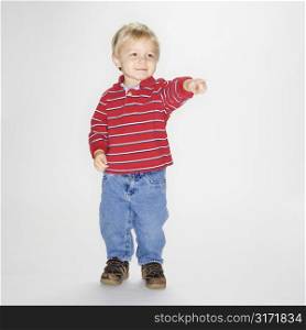 Studio portrait of Caucasian boy standing and pointing against white background.