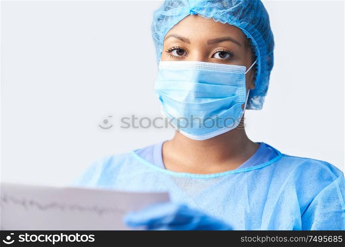 Studio Portrait Of Female Surgeon Wearing Gown And Mask Holding Medical Print Out