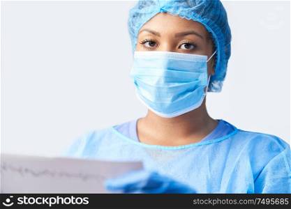Studio Portrait Of Female Surgeon Wearing Gown And Mask Holding Medical Print Out