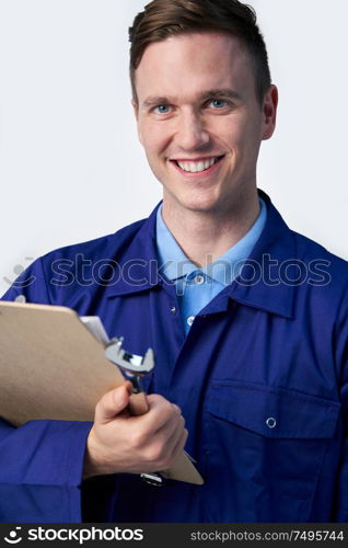 Studio Portrait Of Male Engineer With Clipboard And Spanner Against White Background