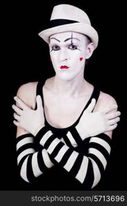 Studio portrait of serious theatrical clown in white hat and striped gloves with red hearts on her face isolated on black background