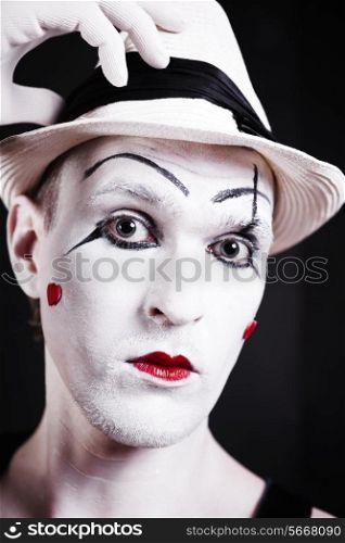 Studio portrait of serious theatrical clown in white hat with red hearts on her face isolated on black background