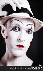 Studio portrait of serious theatrical clown in white hat with red hearts on her face isolated on black background